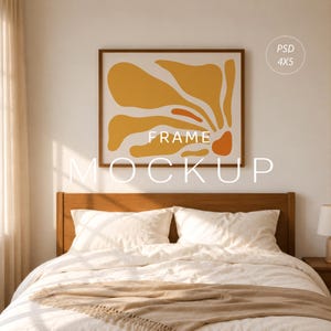 May include: A framed artwork mockup featuring an abstract floral design in shades of yellow and orange against a white background. The frame is brown, and the text "FRAME MOCKUP" is displayed below the artwork. The image is set above a bed with white bedding.