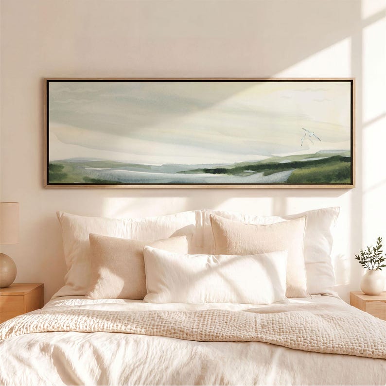 May include: A wide, rectangular landscape painting in a thin wooden frame, featuring soft, blended watercolour washes of pale cream, muted sage green, and light blue, depicting a serene horizon line with a small, faint bird silhouette.