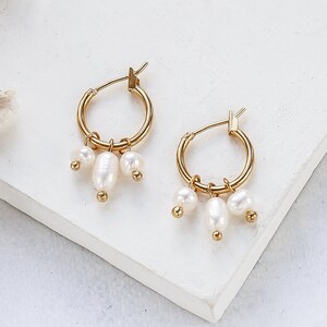 May include: Gold hoop earrings with three small white pearl charms dangling from each hoop.