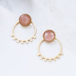 May include: A pair of gold hoop earrings with a pink gemstone in the center of each hoop. The hoops have a decorative scalloped edge.