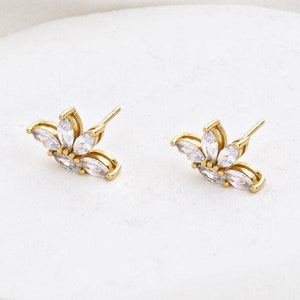 May include: A pair of gold earrings with a cluster of clear cubic zirconia stones in a flower shape.