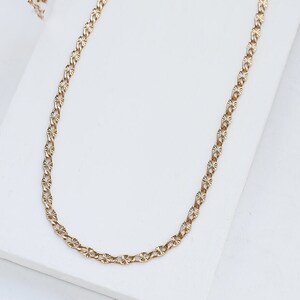 May include: A gold chain necklace with a delicate, patterned design. The chain is made of small, linked ovals with a textured surface.