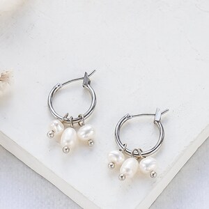 May include: Silver hoop earrings with a cluster of three white pearl charms dangling from each hoop.
