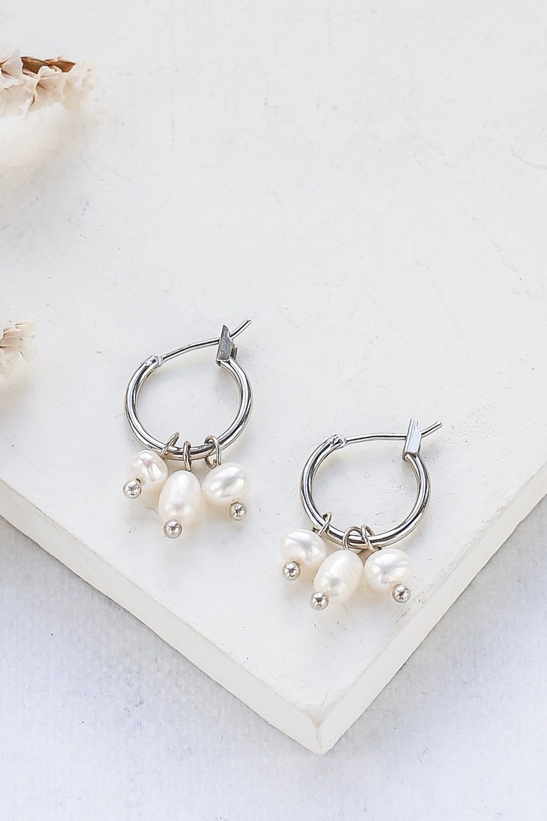May include: Silver hoop earrings with a cluster of three white pearl charms dangling from each hoop.
