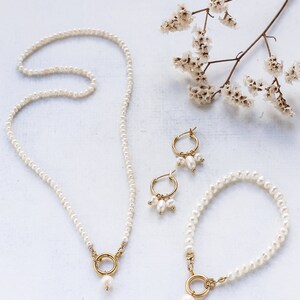 May include: A set of pearl jewelry featuring a necklace, bracelet, and earrings. The necklace and bracelet have a single pearl drop with a gold ring accent. The earrings are hoop style with three pearls dangling from each hoop.