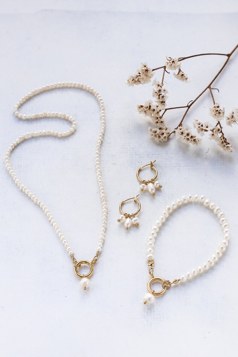 May include: A set of pearl jewelry featuring a necklace, bracelet, and earrings. The necklace and bracelet have a single pearl drop with a gold ring accent. The earrings are hoop style with three pearls dangling from each hoop.