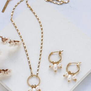 May include: A gold necklace with a circle pendant and three pearl drops. Matching gold hoop earrings with three pearl drops.