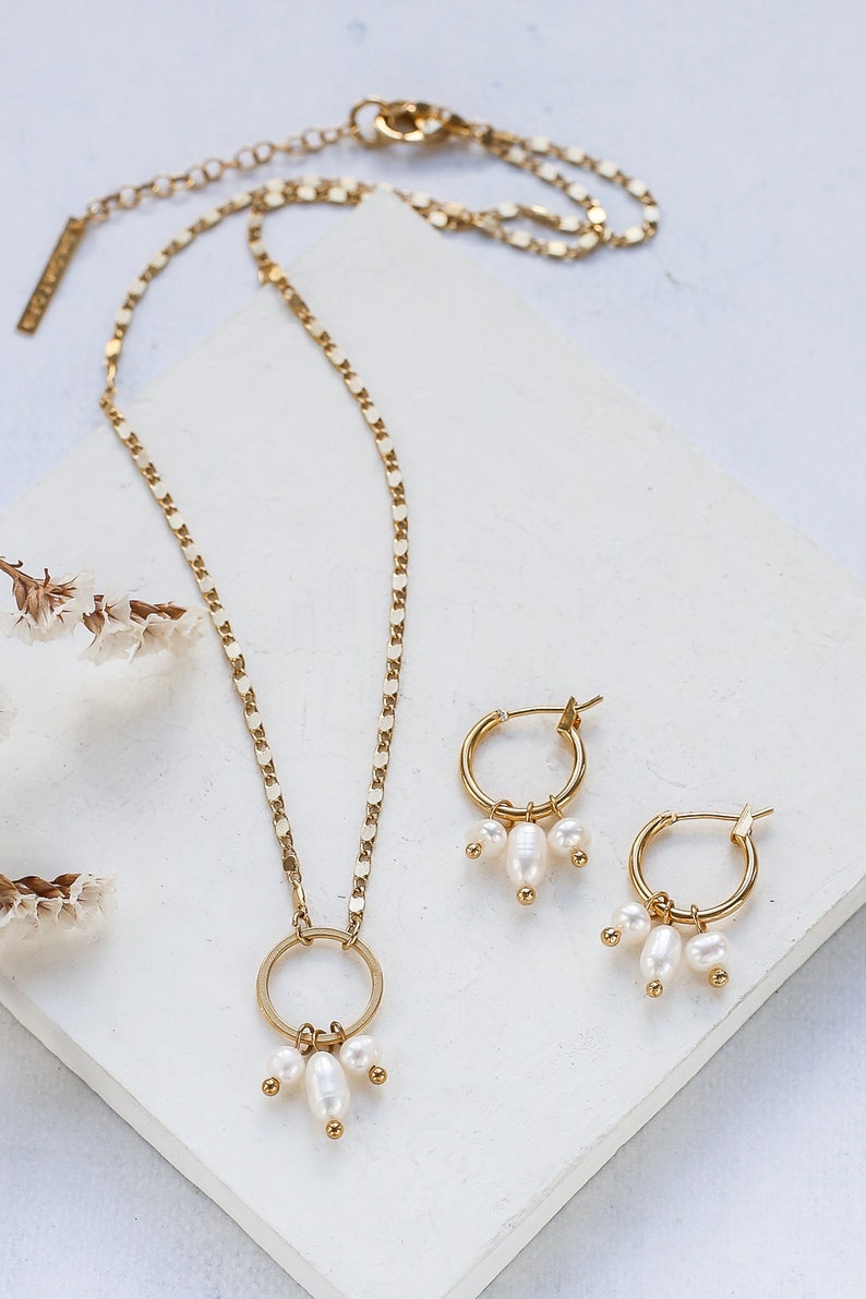 May include: A gold necklace with a circle pendant and three pearl drops. Matching gold hoop earrings with three pearl drops.