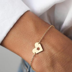 Peut inclure: Un bracelet en chaîne dorée avec un pendentif en forme de cœur comportant une étoile découpée.