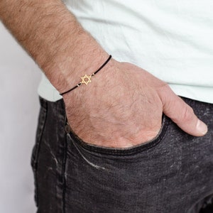 a man wearing a black bracelet with a gold star of david on it