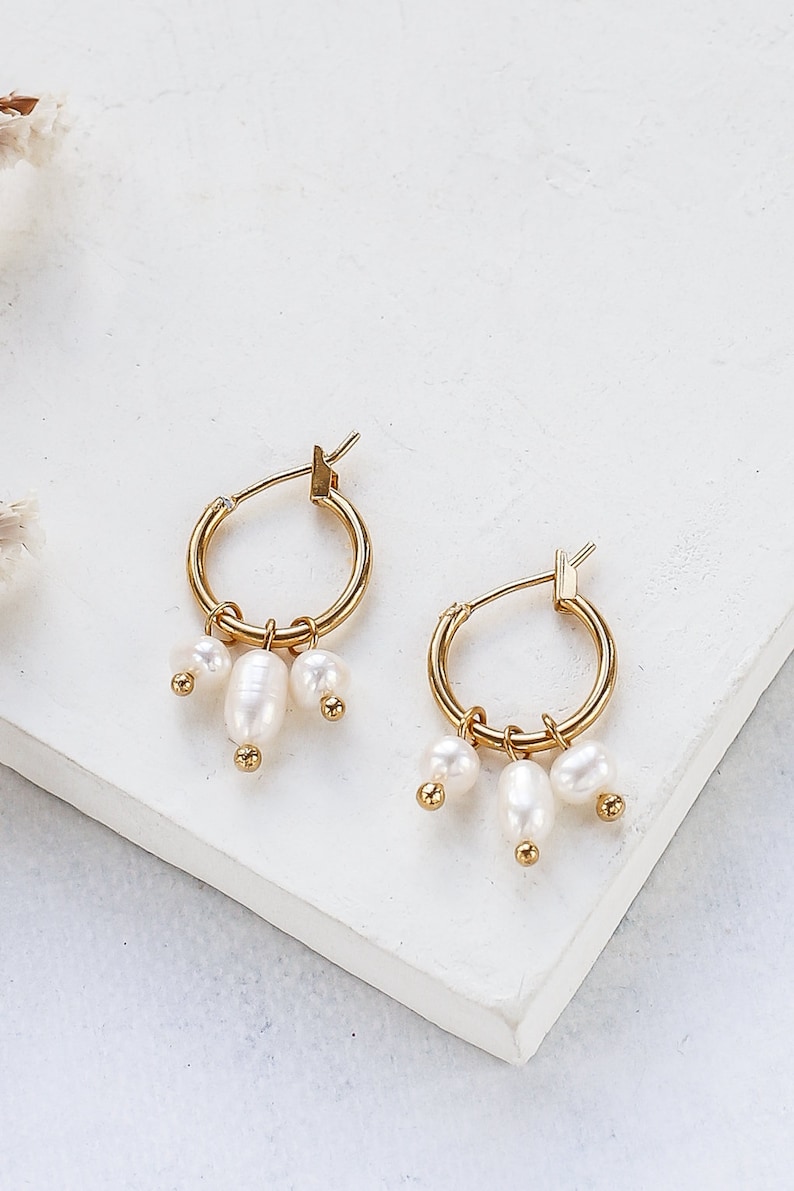 May include: Gold hoop earrings with three small white pearl charms dangling from each hoop.