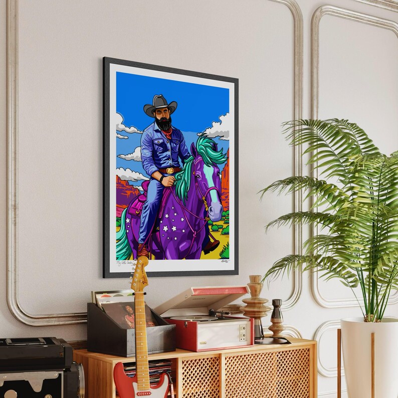 May include: Framed art print featuring a cowboy riding a purple horse with a star pattern. The cowboy wears a denim shirt, blue jeans, and a cowboy hat. The horse has green and purple hair. The background depicts a desert landscape under a blue sky.
