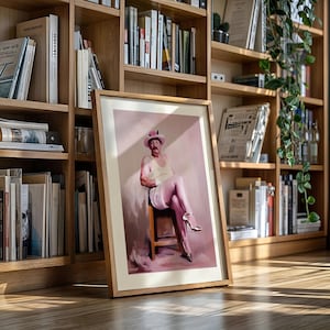 May include: A framed artwork featuring a seated figure in a light-colored outfit and high heels. The portrait has a pink and beige color palette. The artwork is leaning against a wooden bookshelf filled with books.