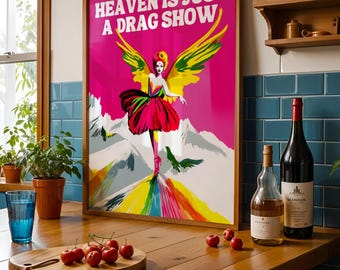 May include: A framed art print with the text "HEAVEN IS JUST A DRAG SHOW" features a drag queen with angel wings against a pink background. The artwork has a rainbow path and mountain backdrop. The print is displayed on a wooden surface.