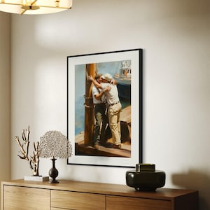 May include: Framed art print depicting two men embracing on a dock, with a boat in the background. The artwork features a warm color palette with blues, browns, and whites. The print is displayed in a black frame.