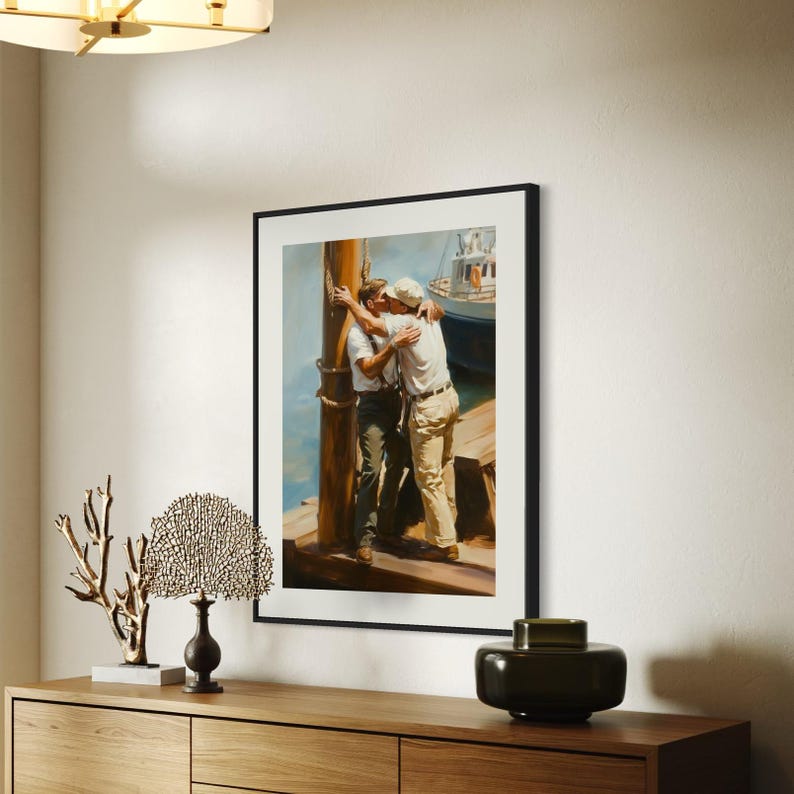 May include: Framed art print depicting two men embracing on a dock, with a boat in the background. The artwork features a warm color palette with blues, browns, and whites. The print is displayed in a black frame.