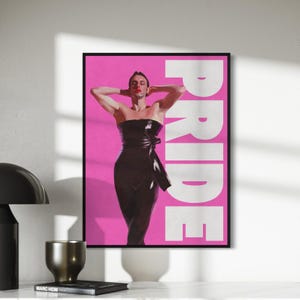 Peut inclure: Une impression d'art numérique représentant une personne vêtue d'une robe noire sans bretelles avec un nœud sur le côté, debout sur un fond rose avec le mot "PRIDE" en lettres blanches.