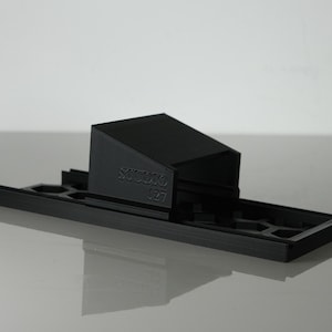 Può includere: Accessorio per fotocamera in plastica nera stampato in 3D con il testo "Studio 127" stampato sul lato.