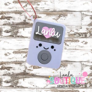 May include: A light purple protective case for a music player with a pink heart and the name "Lanlu" in white script. The case has a smiling face design and a gray control button. A pink lanyard is attached.