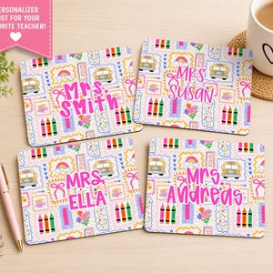 May include: Four square coasters with a school theme, featuring a bus, rainbow, and crayons. Each coaster is personalized with a teacher's name in pink lettering. The coasters are on a light wood surface.
