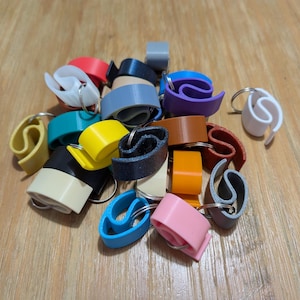 May include: A pile of colorful plastic keychains shaped like the letter 'S'. The keychains are in various colors, including blue, green, yellow, orange, pink, purple, and white.