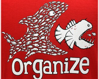 May include: Red t-shirt with a white graphic of a large fish made up of smaller fish being swallowed by a smaller fish with the word "Organize" below.