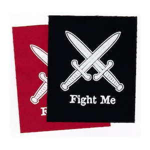 May include: Two iron-on patches with a white crossed swords design and the text "Fight Me". The patch on the left is red and the patch on the right is black.