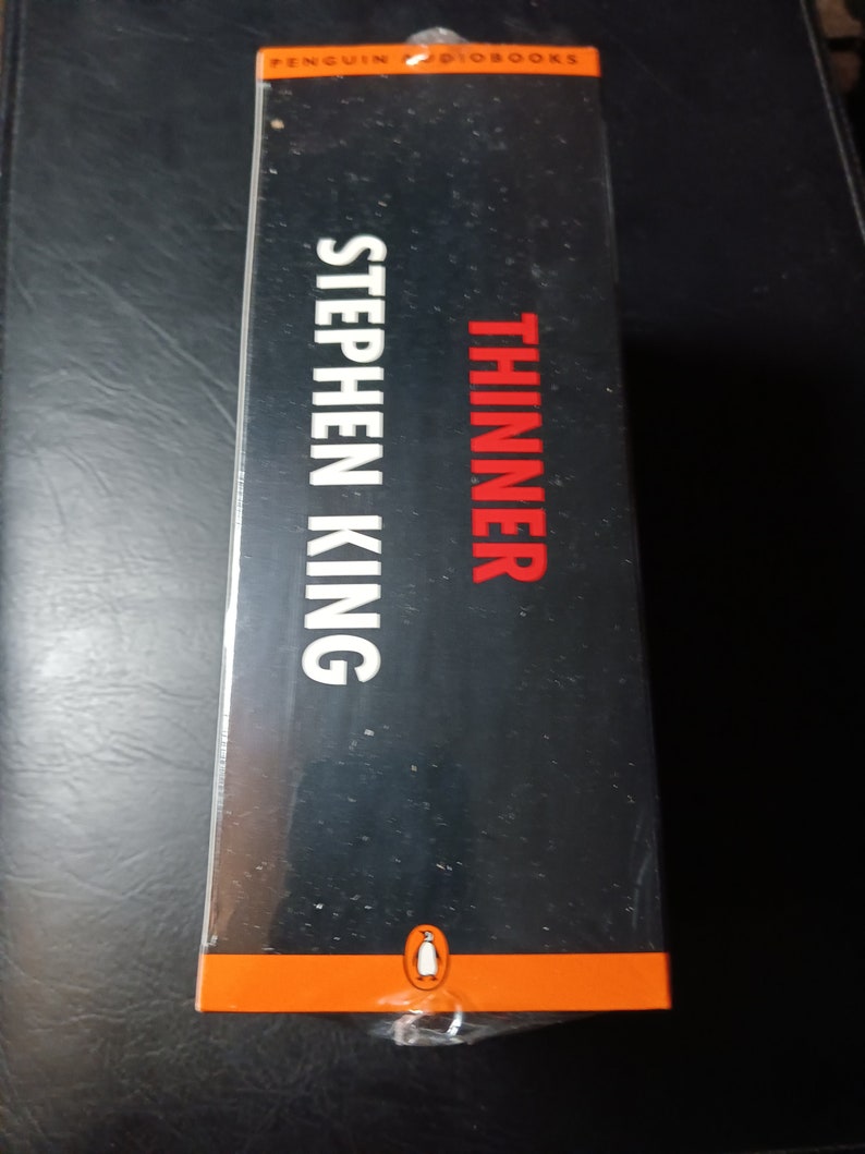May include: A black and orange book cover with the title "Thinner" and the author "Stephen King" in white text. The Penguin Audiobooks logo is at the bottom of the cover.