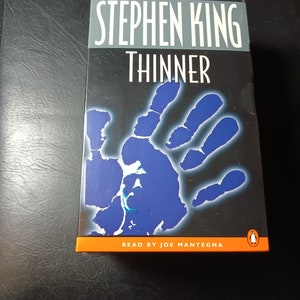 May include: A Penguin Audiobooks audiobook cover featuring a blue handprint with a white outline. The title "Thinner" is in white text on a gray background. The author Stephen King is in white text on a gray background. The text "#1 Bestseller" is in white text on an orange background. The text "Read by Joe Mantegna" is in white text on an orange background. The Penguin logo is in white on an orange background.