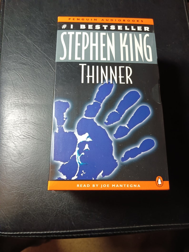 May include: A Penguin Audiobooks audiobook cover featuring a blue handprint with a white outline. The title "Thinner" is in white text on a gray background. The author Stephen King is in white text on a gray background. The text "#1 Bestseller" is in white text on an orange background. The text "Read by Joe Mantegna" is in white text on an orange background. The Penguin logo is in white on an orange background.