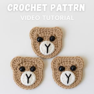 Könnte beinhalten: Drei gehäkelte Bärengesichter mit schwarzen Knopfaugen und weißen und schwarzen "Y"-förmigen Nasen. Die Bären sind hellbraun und auf weißem Hintergrund angeordnet. Der Text "CROCHET PATTRN VIDEO TUTORIAL" befindet sich oben im Bild.