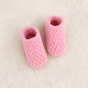 Op de afbeelding: Een paar zachte roze pantoffels met een textuur met een bubbelachtig patroon. De pantoffels zijn gemaakt van een zacht materiaal en zijn ontworpen voor binnenshuis. Het open ontwerp maakt het gemakkelijk om aan en uit te trekken.