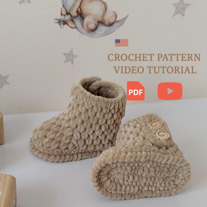 Op de afbeelding: Een paar beige gehaakte babyslofjes met een textuurontwerp. De slofjes hebben houten knopen en worden weergegeven met de tekst "CROCHET PATTERN VIDEO TUTORIAL" en een PDF-pictogram.