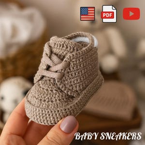 May include: A crocheted baby sneaker in a neutral tan color. The tiny shoe has laces and a white trim around the ankle. The words "BABY SNEAKERS" are printed at the bottom of the image.