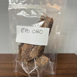 Puede incluir: Una bolsa de plástico transparente con una etiqueta blanca que dice "EPO OBO" y contiene trozos marrones y secos que parecen corteza.