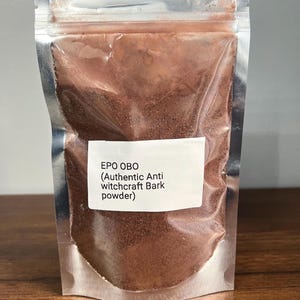 Puede incluir: Una bolsa transparente y sellada que contiene polvo marrón. Una etiqueta blanca en la parte delantera dice "EPO OBO (Authentic Anti witchcraft Bark powder)". La bolsa está hecha de un material metálico brillante y está sellada en la parte superior.