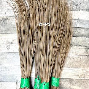 May include: Three brown brooms with green plastic ties. The brooms are made of natural fibres and are tied together at the top.