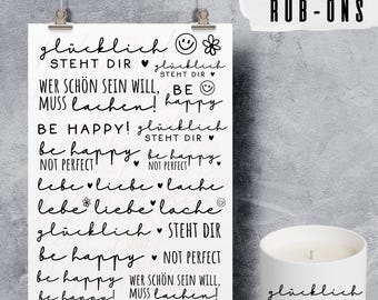 May include: A white print with black text, including phrases like "Be Happy" and "Love, Laugh, Live", is displayed. A white candle with the words "glücklich STEHT DIR" is next to the print. The words "RANDLOSE RUB-ONS" are at the top.
