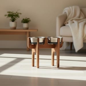 Puede incluir: Un soporte de madera para cuencos para mascotas con dos cuencos de acero inoxidable. El soporte es de madera marrón claro y tiene un diseño simple y moderno. Los cuencos están elevados.