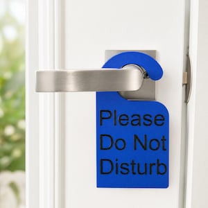 May include: A bright blue door hanger sign with a hook shape at the top, hanging from a brushed silver metal door handle. The sign features the black text "Please Do Not Disturb" printed in a clear, sans-serif font on the front surface.