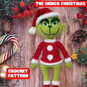 Könnte beinhalten: Häkelanleitung für eine grüne Grinch-Puppe, die ein rotes Weihnachtsmannkostüm mit weißen Verzierungen trägt. Die Puppe sitzt auf einer Holzoberfläche mit Weihnachtsdekoration.