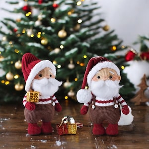 Può includere: Due figure di Babbo Natale all'uncinetto con camicie a righe rosse e bianche, pantaloni marroni e barbe bianche. Sono in piedi davanti a un albero di Natale con decorazioni rosse e bianche.