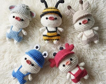 May include: Five handmade crochet dolls in various animal costumes. The dolls are white with black eyes and pink beaks. Costumes include a mouse, bee, bunny, frog, and a doll with heart-shaped ears. Each doll wears overalls in different colors.