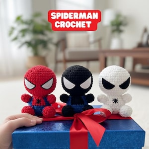 May include: Three crocheted Spider-Man figures in red, black, and white, each with a unique mask design. The figures are seated on a blue gift box with a red ribbon. The text "SPIDERMAN CROCHET" is displayed above.