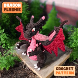 May include: Crochet pattern for a red and brown dragon plushie. The dragon has pink accents and a large, red wing. The pattern is available for download.