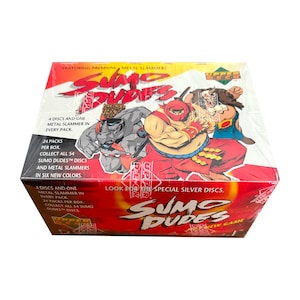 May include: A red, white and black box with the words "Sumo Dudes" printed on it. The box features a cartoon image of a sumo wrestler in a red and black outfit. The box also includes the text "Featuring Premium Metal Slammers" and "Look for the Special Silver Discs."
