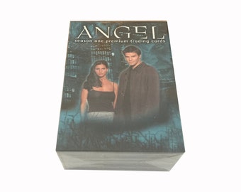 Pode incluir: Uma caixa de cartas de troca premium da primeira temporada de Angel com uma foto dos personagens principais na frente. A caixa é azul e preta com um horizonte da cidade no fundo.