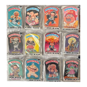 Peut inclure: Une collection de douze badges Garbage Pail Kids, chacun emballé individuellement dans du plastique transparent. Chaque badge présente une illustration de personnage colorée avec le texte Garbage Pail Kids et Net Contents One Button.