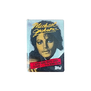 May include: A vintage trading card pack featuring Michael Jackson. The pack has a portrait of Michael Jackson with the name in gold lettering. The pack includes 3 super gloss photo cards, 3 stickers, and 1 stick of bubble gum.