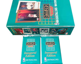 May include: A teal Skybox Series II NBA basketball card box set with two packs of Inaugural Edition cards. The box features images of basketball players and the text "NBA BASKETBALL CARDS 1990-91 SEASON". The packs read "5 NBA TRADING CARDS".